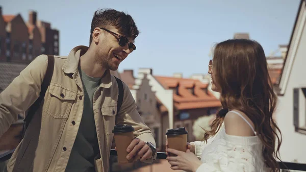 Stilvolles Paar lächelt, während es Pappbecher draußen hält — Stockfoto