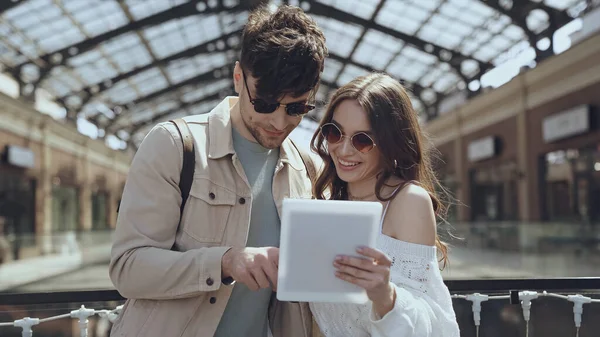 Couple in sunglasses smiling while using digital tablet in shopping mall — Photo de stock