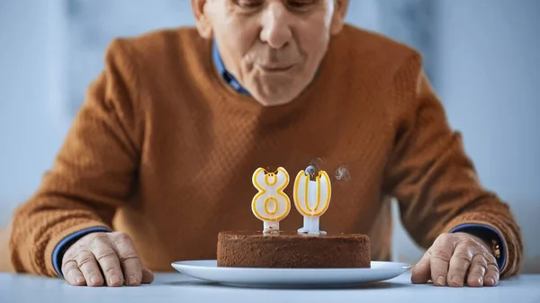 Alegre anciano soplando velas en pastel de cumpleaños sobre fondo gris - foto de stock