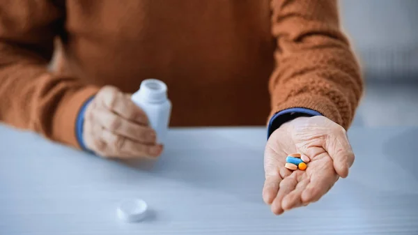 Закрытый вид банка медицины и разноцветные таблетки в руках пожилого человека на сером фоне — стоковое фото