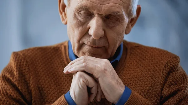 Retrato de anciano con los ojos cerrados y las manos cerradas cerca de la cara sobre fondo gris - foto de stock