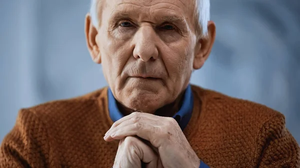 Ritratto di uomo anziano con le mani serrate vicino al volto su sfondo grigio — Foto stock