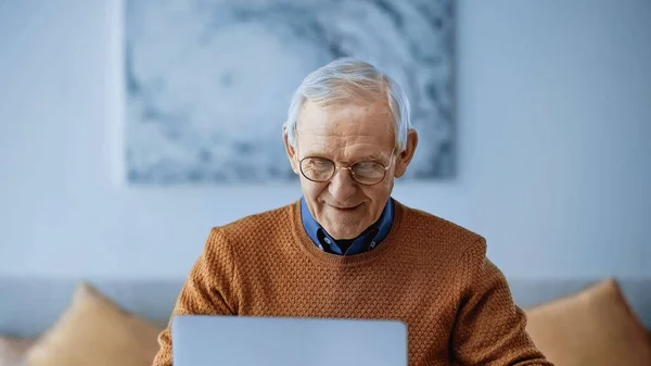 Homme âgé souriant travaillant sur ordinateur portable dans le salon moderne — Photo de stock