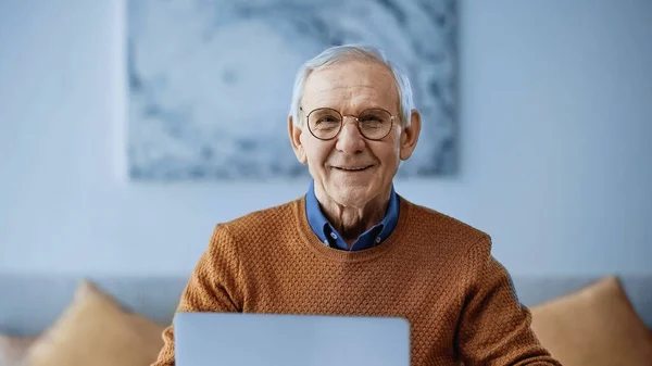 Улыбающийся пожилой мужчина сидит дома с ноутбуком — стоковое фото