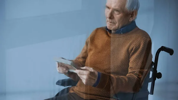 Verträumter Senior im Rollstuhl mit Familienbild auf grauem Hintergrund — Stockfoto