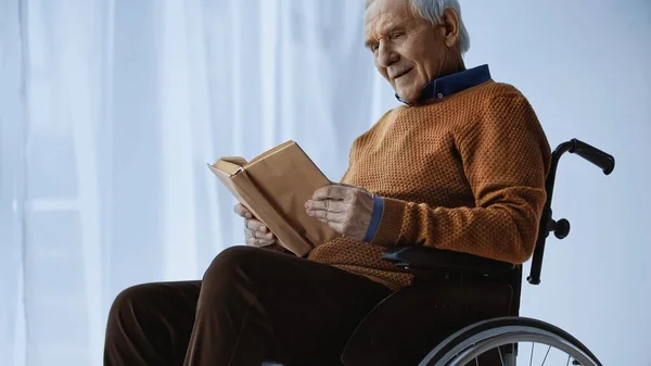 Старший мужчина сидит в инвалидной коляске и читает книги в доме престарелых — стоковое фото