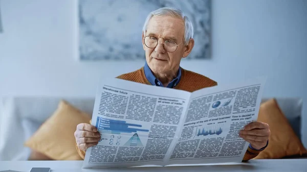 Uomo anziano in occhiali che legge il giornale nel salotto moderno — Foto stock
