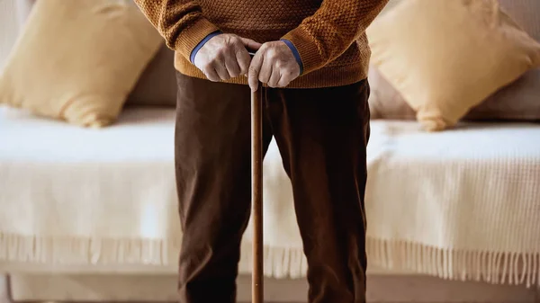 Cropped view elderly man with walking stick standing near sofa at home — Stock Photo