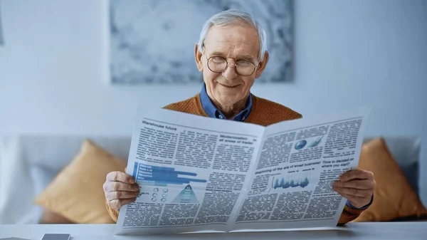 Sorridente uomo anziano in occhiali leggere giornale a casa — Foto stock