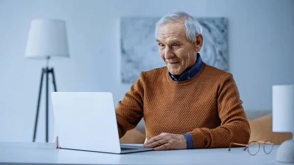 Hombre de edad avanzada asombrado mirando portátil en la sala de estar - foto de stock