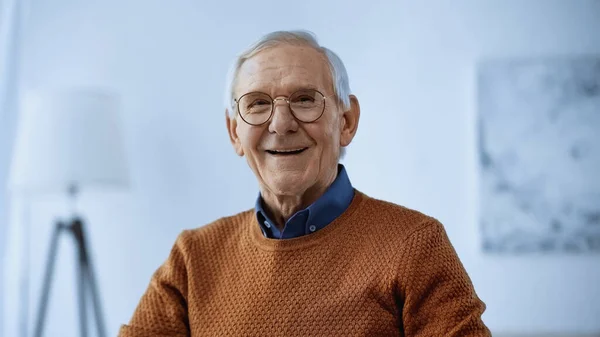 Lächelnder älterer Mann mit Brille blickt in modernes Wohnzimmer in die Kamera — Stockfoto