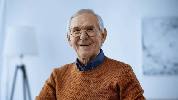 Anciano sonriente en gafas mirando a la cámara en la sala de estar moderna - foto de stock
