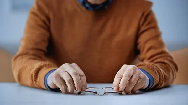 Cropped view of elderly man holding glasses in hands on grey and beige background — Stock Photo