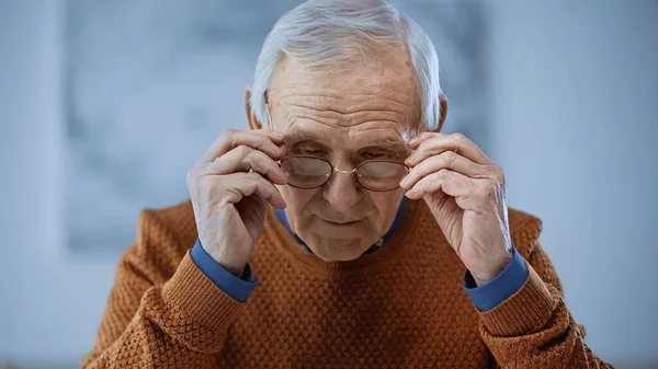 Anciano concentrado ajustando gafas sobre fondo gris - foto de stock