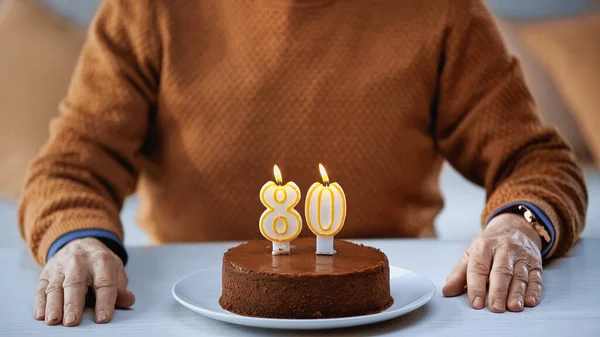 Partial view of elderly man sitting in front of birthday cake with candles at home — Stock Photo