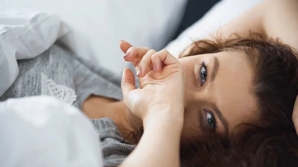 Jovem mulher encaracolado cobrindo rosto com a mão enquanto deitado na cama de manhã — Fotografia de Stock