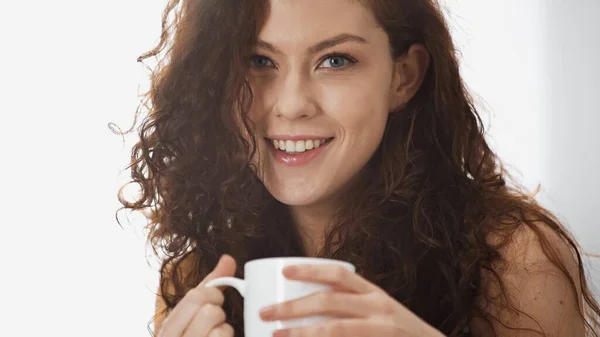 Mujer sonriente y rizada sosteniendo la taza de café en la mañana - foto de stock
