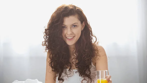 Feliz joven mujer sosteniendo vaso de jugo de naranja en la mañana - foto de stock
