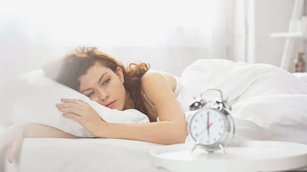 Awake young woman looking at retro alarm clock — Stock Photo