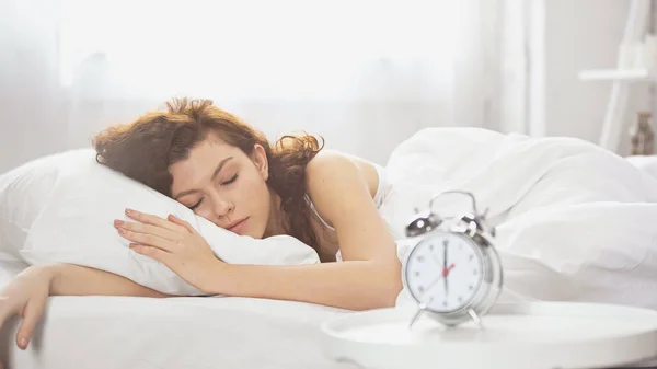 Mujer joven y rizada durmiendo cerca del despertador retro - foto de stock