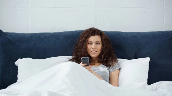 Щаслива молода жінка тримає пульт дистанційного керування в ліжку — стокове фото