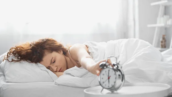 Displeased young woman reaching retro alarm clock in morning — Stock Photo