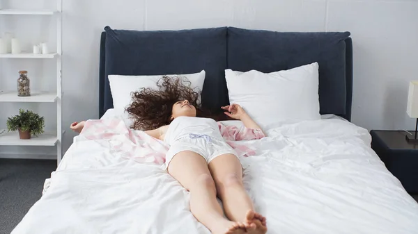 Encaracolado e descalço mulher deitada na cama em casa — Fotografia de Stock