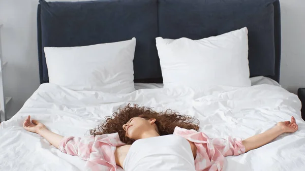 Lockige und lächelnde Frau entspannt sich zu Hause auf dem Bett — Stockfoto