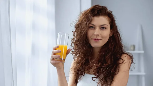 Rizado joven mujer sosteniendo vaso de jugo de naranja en casa - foto de stock