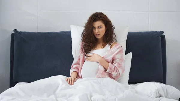 Pregnant woman touching belly while sitting in bed — Stock Photo