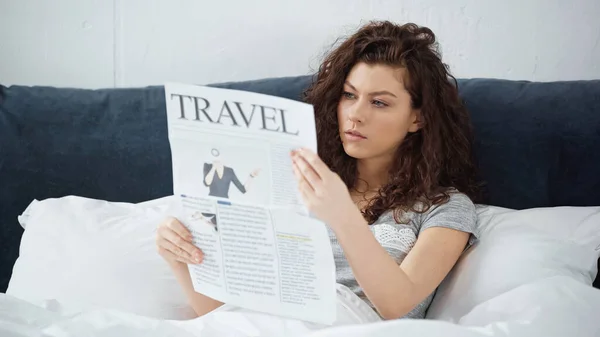 Lockige junge Frau liest Reisezeitung im Schlafzimmer — Stockfoto