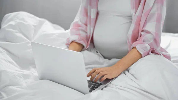 Обрезанный вид беременной фрилансеры с помощью ноутбука в спальне — стоковое фото