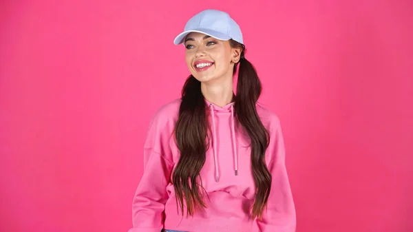 Усміхнена молода доросла жінка в шапці і светрі дивиться ізольовано на рожевому — стокове фото