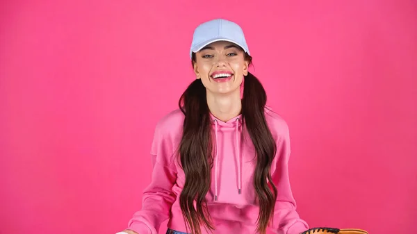 Smiling young adult woman in cap and hoodie looking at camera isolated on pink - foto de stock