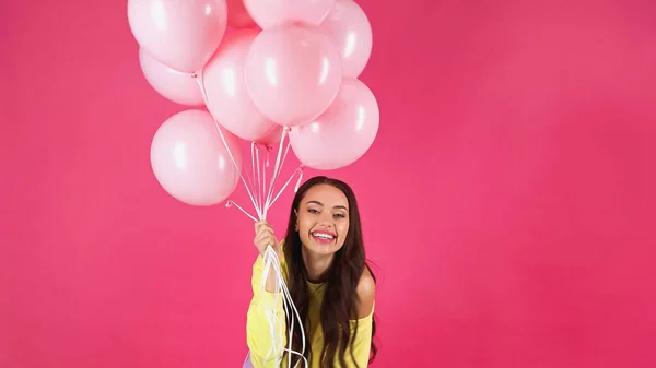 Fröhliche junge erwachsene Frau in gelbem Sweatshirt mit Luftballons auf rosa — Stockfoto