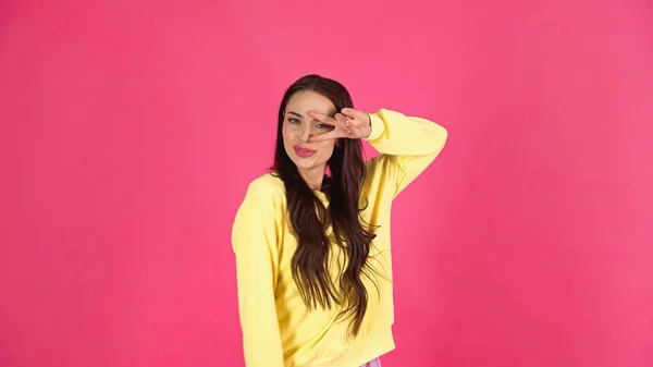 Playful young adult woman with peace gesture near face isolated on pink - foto de stock