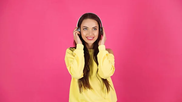 Pretty young adult woman holding hands on headphones while listening music isolated on pink — Fotografia de Stock