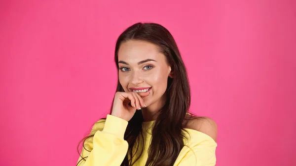 Shy young adult woman looking at camera with finger near mouth isolated on pink — Photo de stock