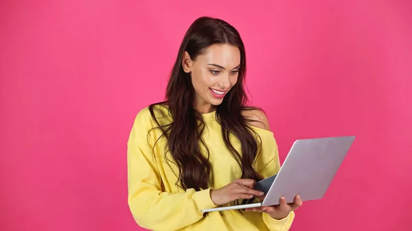 Lächelnde junge erwachsene Frau tippt auf Laptop und hält Kreditkarte isoliert auf rosa — Stockfoto