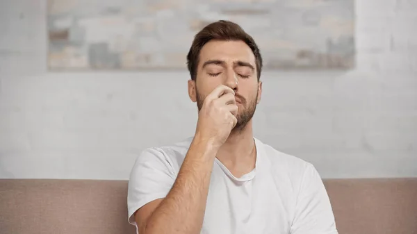 Allergic man with closed eyes using nasal spray at home — Fotografia de Stock