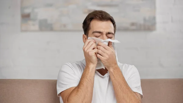 Allergic man sneezing in napkin at home — Stock Photo
