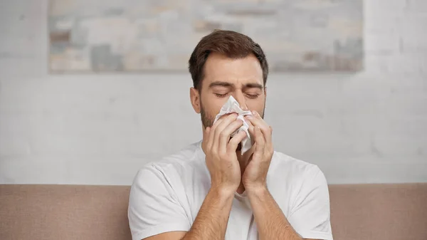 Man with pollen allergy sneezing in napkin at home — Stock Photo