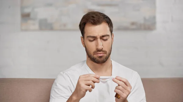 Bearded man holding electronic thermometer at home — Foto stock