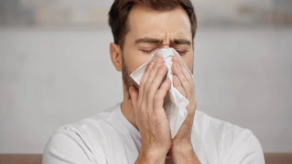 Man with allergy sneezing in napkin at home — Stock Photo