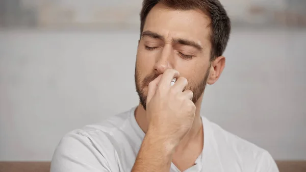 Allergic man in white t-shirt using nasal spray at home — Fotografia de Stock