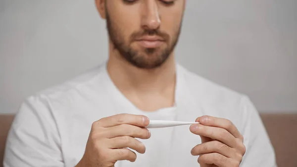 Cropped view of blurred man holding electronic thermometer at home — Stock Photo