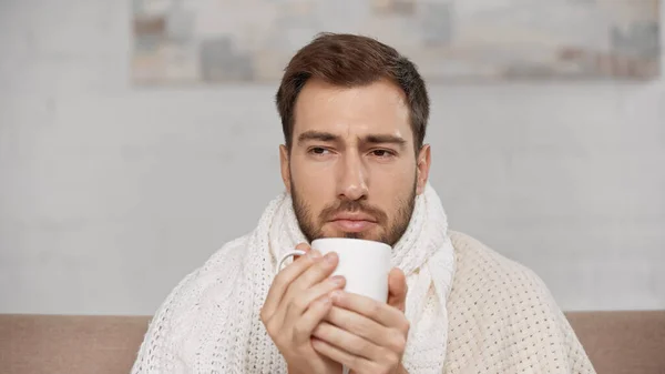 Sick man wrapped in blanket holding cup of tea — Fotografia de Stock