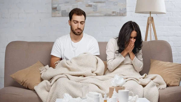 Kranke Frau niest neben Mann und Flaschen mit Tabletten auf Couchtisch — Stockfoto