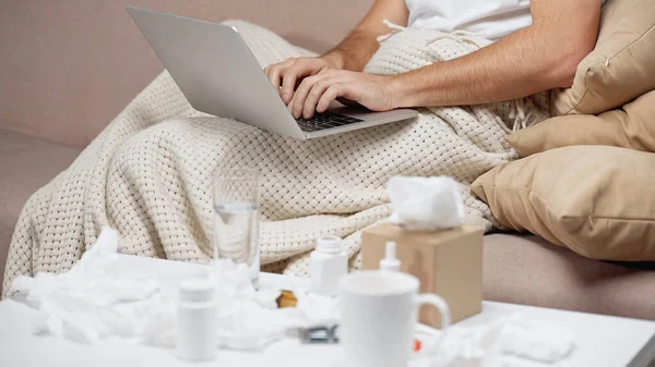 Ausgeschnittene Ansicht eines Mannes, der auf Laptop neben Medikamenten auf Couchtisch tippt — Stockfoto