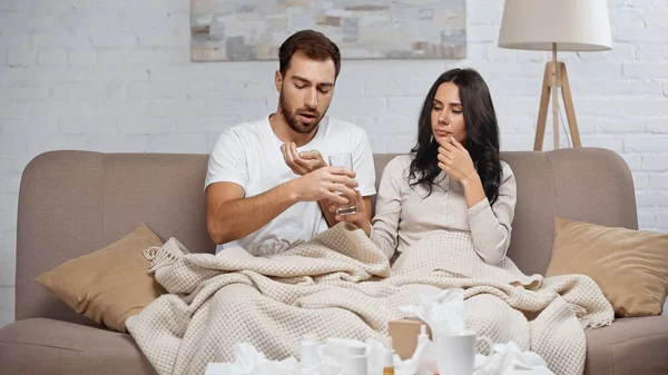 Caring woman giving glass of water to sick man in living room — Foto stock